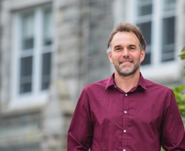 A photo of Dr. Alexander MacLeod standing behind MacNally Building SMU