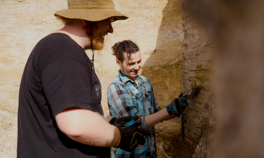 Two students brush a wall at an archelogical site in Italy